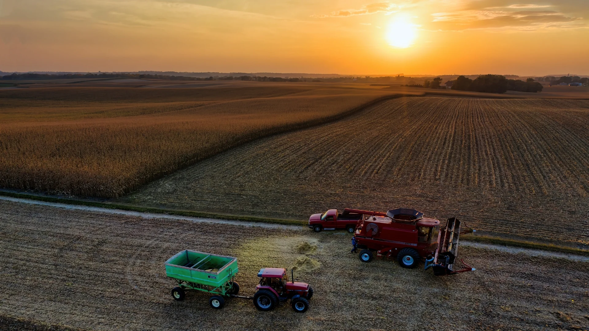 Case IH combine and tractor beside a harvested field at sunset